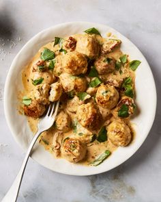 a white plate topped with meatballs covered in sauce and garnished with green leaves