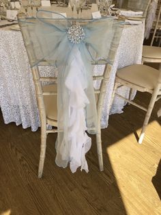 the table is set with white linens and blue ribbons on it, along with silver place settings