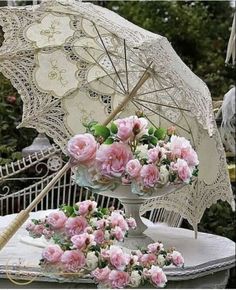 pink flowers are arranged in a vase on a table with an umbrella and lace doily