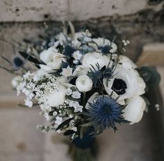 a bouquet of white and blue flowers in front of a brick wall with water droplets on it