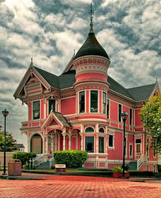 a large pink house with a tower on the top and two stories down the middle