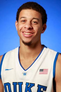 a young man wearing a white and blue basketball uniform smiling at the camera with an american flag on his jersey