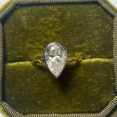 a diamond ring sitting on top of a velvet cushion in a green box with gold trim around it