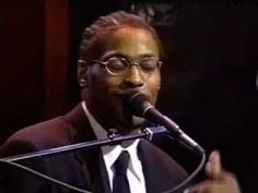 a man wearing glasses and a suit speaking into a microphone