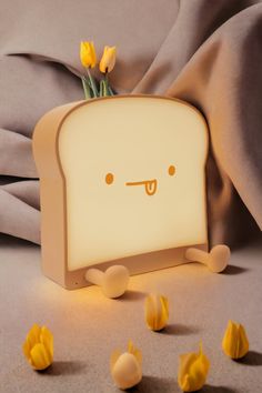 a toaster shaped like a face with yellow flowers in front of it on a gray surface