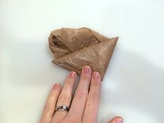 two hands holding a piece of brown paper on top of a table next to each other