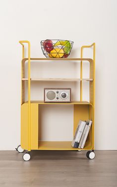 a yellow cart with books and a basket on top is shown in front of a white wall