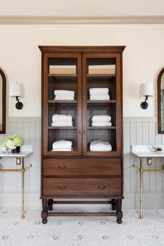 a wooden cabinet with white towels on top of it in a bathroom next to two sinks