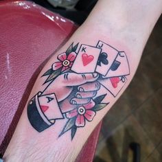 a tattoo on the arm of a man with playing cards and flowers in his hand