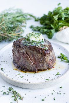 a piece of steak is sitting on a plate with herbs around it and some parsley in the background