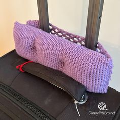 a purple knitted bag sitting on top of a black piece of luggage with handles