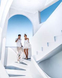 a man and woman are walking down the stairs in an artistic white building with blue sky behind them