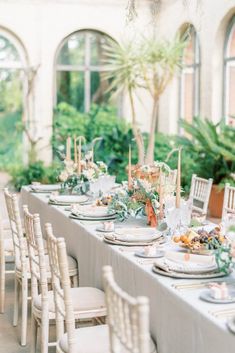 a long table is set with white chairs and place settings for an outdoor dinner party