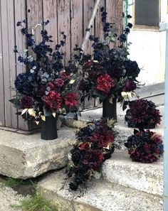 three black vases filled with flowers sitting on steps