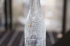 a glass bottle with writing on it sitting on top of a table next to a window