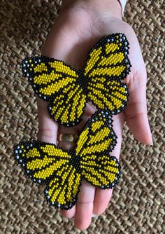 two yellow and black beaded butterfly brooches on a person's hand