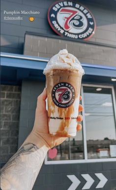 a person holding up a cup of coffee in front of a restaurant