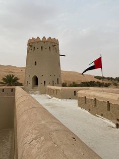 a flag flying in the wind next to a castle like structure with sand and water