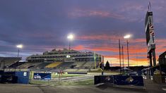 an empty football stadium at sunset with the sun going down in the distance and lights on