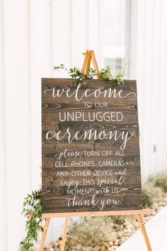 a wooden sign that says we welcome our unplugged ceremony with greenery