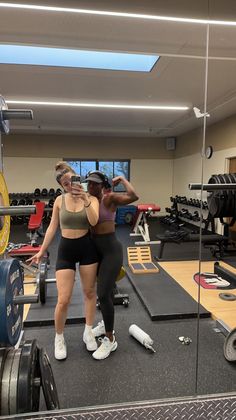 two women in a gym doing squats with dumbbells and barbells