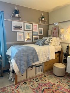 a bed sitting in a bedroom next to a window with blue curtains and pictures on the wall