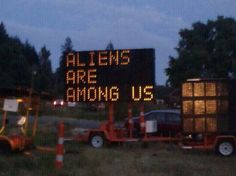 there is a sign that says aliens are among us on the side of the road