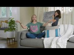 two women sitting on a couch in a living room with pillows and blankets around them