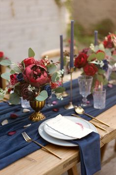 the table is set with blue linens and red flowers in vases on it