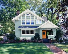 a gray and white house with yellow door in the front yard on a sunny day