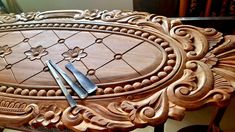 an ornate wooden table with two knives and fork on it's side, in front of a mirror