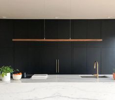 a kitchen with black cabinets and white marble counter tops is pictured in this image, there are potted plants next to the sink