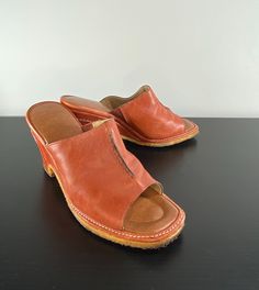 "Such great pumpkin colored leather wedge slides from the 1970s. Love the seaming details and the crepe sole! Very comfy and adorable. Lined upper. Cushioned inner sole. Label: (Hard to read) Revelation Made in the U.S.A. Leather Upper 7M Condition is good. There are some stains on the leather throughout, see pictures. The lining of the leather upper seems to be flaking off in dusty powder. Measurements: Length: 9 1/2\" Width at widest point of toe box: 3 3/8\" Heel height: 3 3/8\" (CB of heel) Retro Closed Toe Leather Mules, Retro Leather Closed Toe Mules, Retro Leather Platform Mules, Vintage Brown Mules With Leather Sole, Retro Leather Mules With Round Toe, Vintage Brown Mules For Summer, Retro Leather Clogs For Spring, Retro Leather Mules For Spring, Vintage Summer Clogs With Round Toe