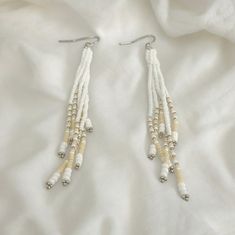 Crafted with meticulous attention to detail, these White and Cream Fringe Earrings are an exquisite blend of creativity and elegance. The cream fringe dances playfully, adding a touch of bohemian charm that is perfect for any festival or special occasion. Handmade with Creative Beadwork, these earrings are a true testament to artisanal craftsmanship. Perfect for gifting, these Seed Bead Fringe Earrings are a beautiful option for Mother's Day or any celebration. The delicate seed beads intertwine White Beaded Necklaces With Dangling Beads, White Dangle Beaded Necklaces, Adjustable White Jewelry With Dangling Beads, White Beaded Necklace With Dangling Beads, White Adjustable Jewelry With Dangling Beads, Adjustable White Beaded Necklace With Dangling Beads, White Beaded Drop Earrings With Tiny Beads, White Beaded Earrings With Dangling Beads For Wedding, White Silver Beads For Jewelry Making