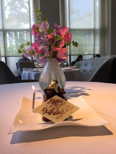 a birthday card is placed on a plate with a candle and flowers in a vase