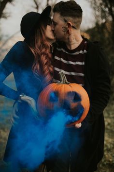 a man and woman kissing while holding a pumpkin