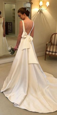 a woman in a wedding dress looking at herself in the mirror with her back to the camera