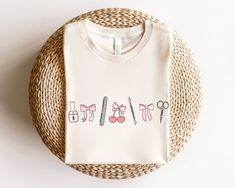 a white t - shirt with scissors and bow ties on it sitting next to a wicker basket