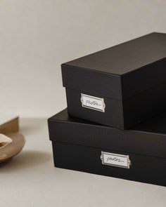 two black boxes sitting next to each other on top of a white table with a pair of shoes