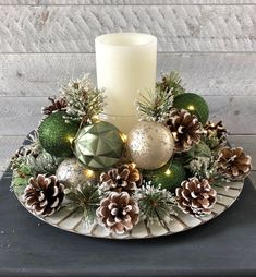 a white candle sitting on top of a plate with pine cones and christmas ornaments around it