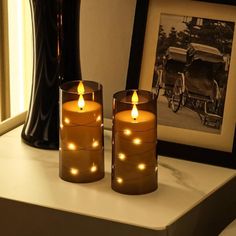 two lit candles sitting on top of a table next to a framed photograph and vase