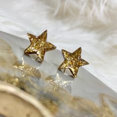 These resin star stud earrings are the perfect addition to your look. Featuring a glittery gold finish, these earrings have 18K gold plated and nickel free posts Trendy Gold Earrings With Star Charm, Trendy Gold Glitter Earrings, Trendy Glitter Gold Earrings, Gold Starburst Earrings For Party, Star Shaped Glitter Earrings For Party, Gold Starburst Party Earrings, Gold Star-shaped Earrings For Party, Gold Star-shaped Sparkling Jewelry, Gold Sparkling Star Jewelry