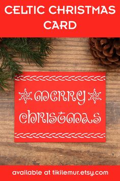 a red christmas card sitting on top of a wooden table with pine cones and evergreen branches