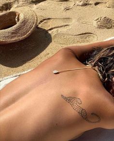 a woman laying on top of a sandy beach next to a straw hat and umbrella