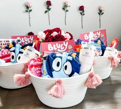 three baskets filled with toys and candy on top of a wooden table next to flowers