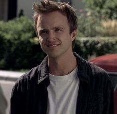 a man standing in front of a red car and smiling at the camera with his hand on his hip