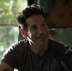 a man sitting in front of a microphone and smiling at the camera while wearing a gray t - shirt