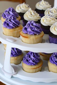 cupcakes with purple frosting and sprinkles on a white cake stand