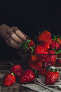 a person picking strawberries from a glass bowl