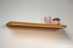 two pink vases sitting on top of a wooden shelf next to a glass cup